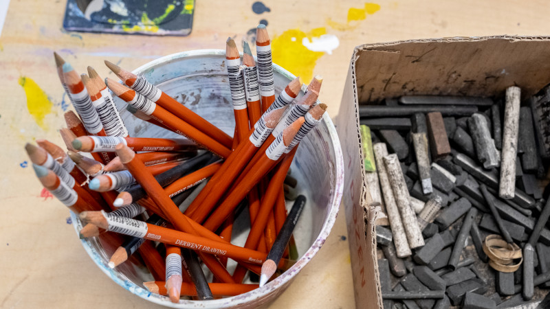 Bucket of colored pencils and box of charcoal sitting on table
