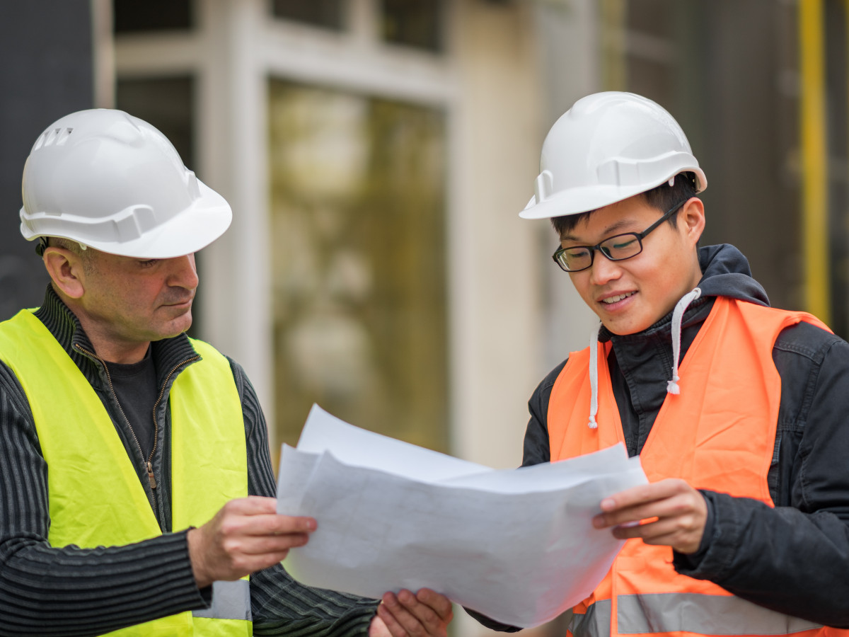 Construction worker and intern look at a paper