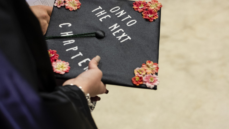 Graduate holding mortar board cap with lettering