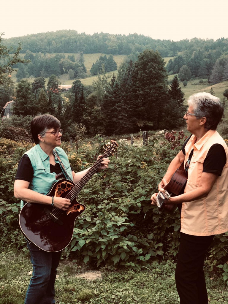 Emily and Lynn in backyard raspberry patch playing guitar
