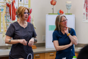 Two students listen to their instructor during a medical assisting lab.