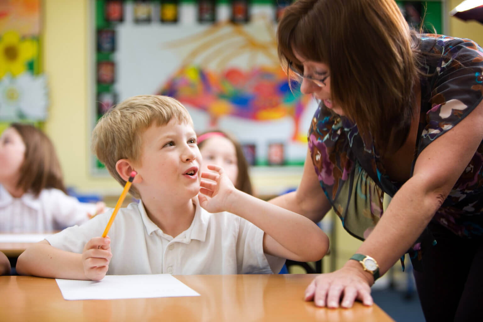 A moment of understanding from a young primary school pupil beginning to understand his subject with a little help from his teacher in the classroom.