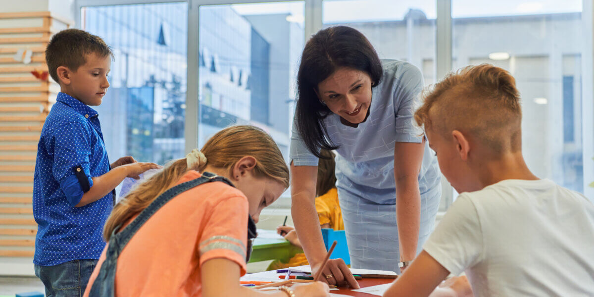 Creative kids during an art class in a daycare center or elementary school classroom drawing with female teacher.