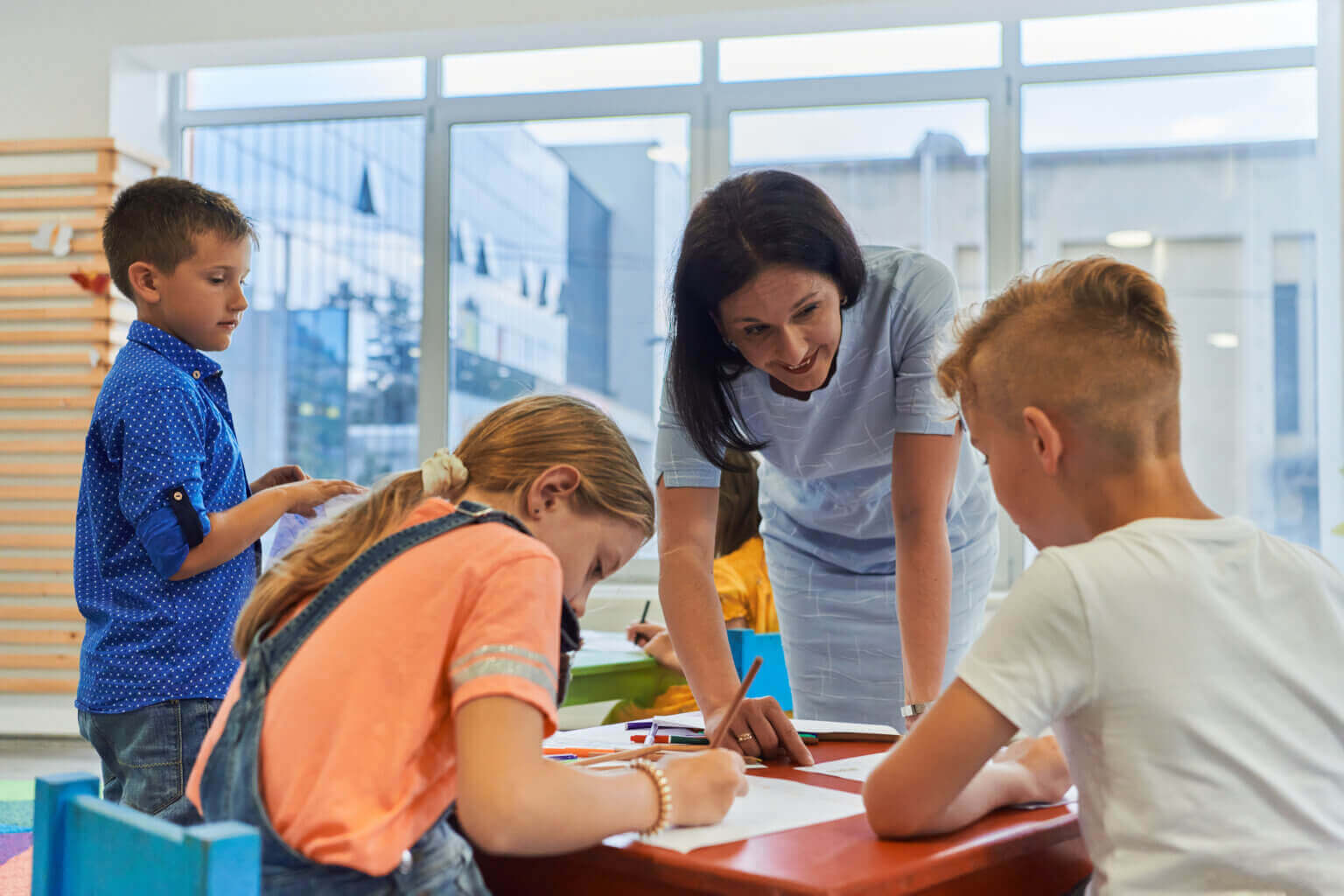 Creative kids during an art class in a daycare center or elementary school classroom drawing with female teacher.