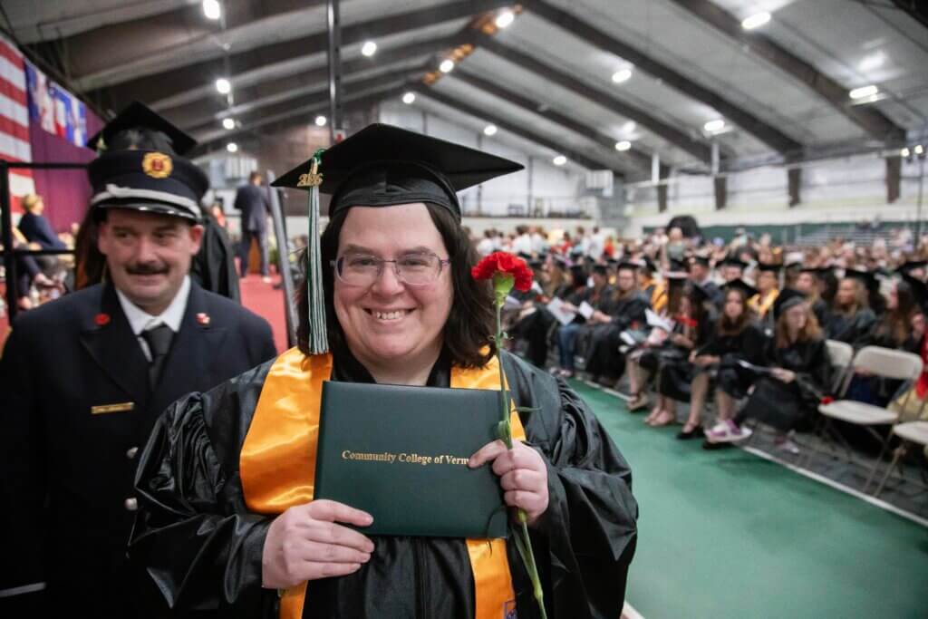 A CCV graduate in cap and gown holds up her diploma cover.