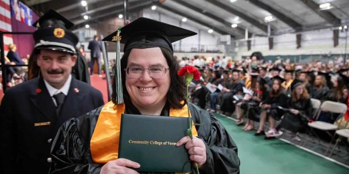 A CCV graduate in cap and gown holds up her diploma cover.
