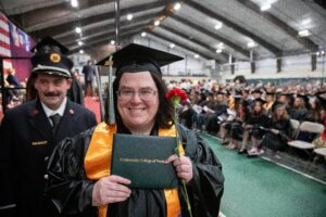 A CCV graduate in cap and gown holds up her diploma cover.