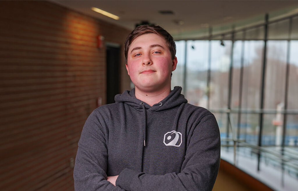 Collin Clair in a gray hooded sweatshirt with his arms crossed.