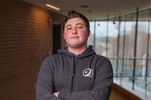 Collin Clair in a gray hooded sweatshirt with his arms crossed.