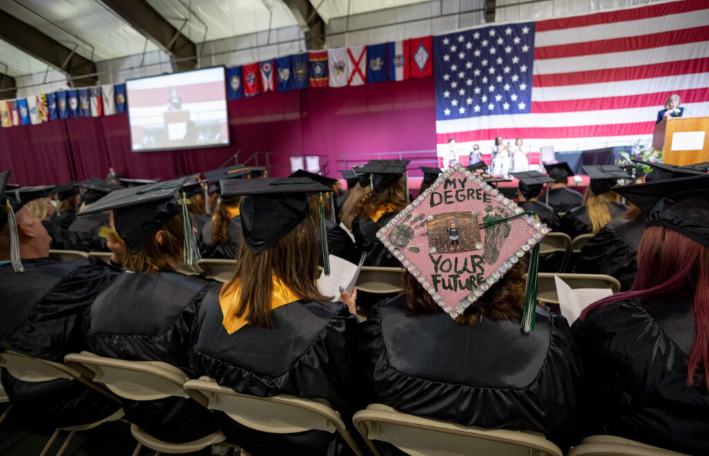 CCV graduates seated at commencement. One mortar board reads "My Degree Your Future."