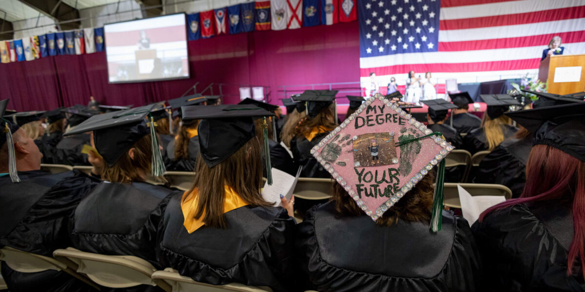 CCV graduates seated at commencement. One mortar board reads "My Degree Your Future."