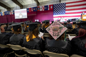 CCV graduates seated at commencement. One mortar board reads "My Degree Your Future."